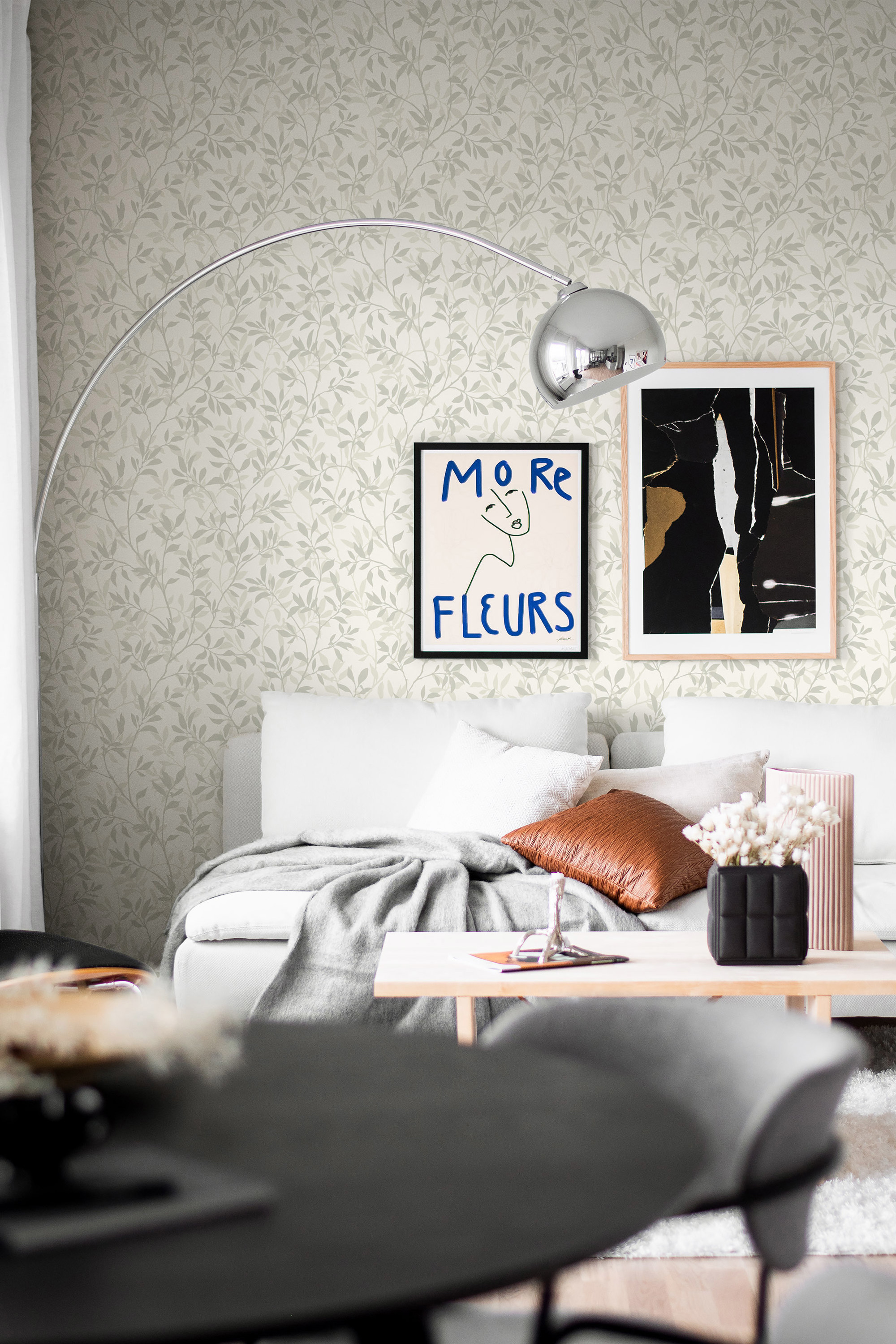 Ett vardagsrum med grönblommig tapet, soffa med en pläd slängd på. 