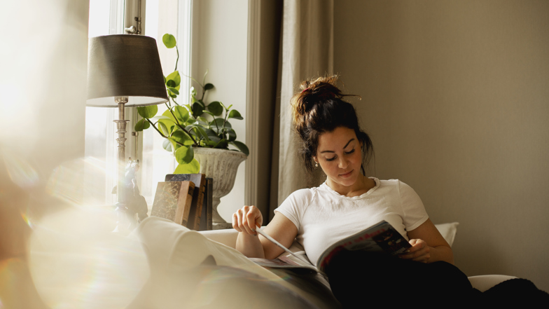 Kvinna njuter i sin soffa med en bok i knät.