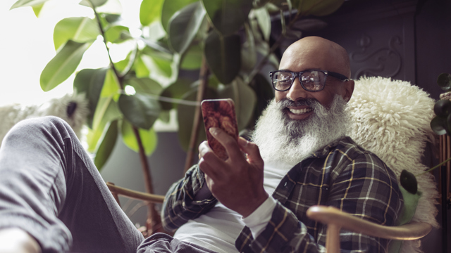 En man sitter bekvämt i sin fåtölj och läser på sin smartphone. 