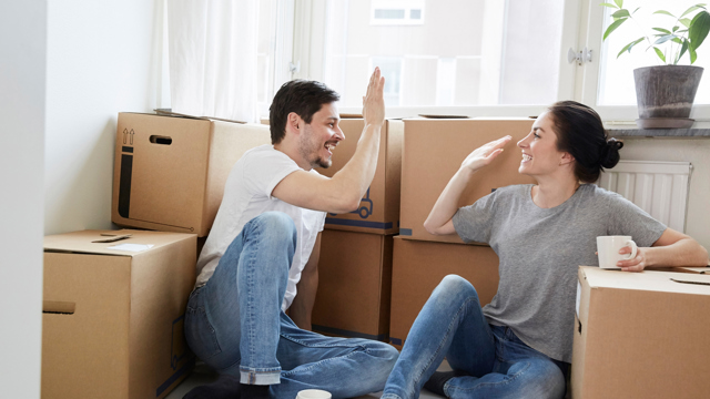 Ett ungt par gör high five sittandes på golvet bland massa flyttkartonger