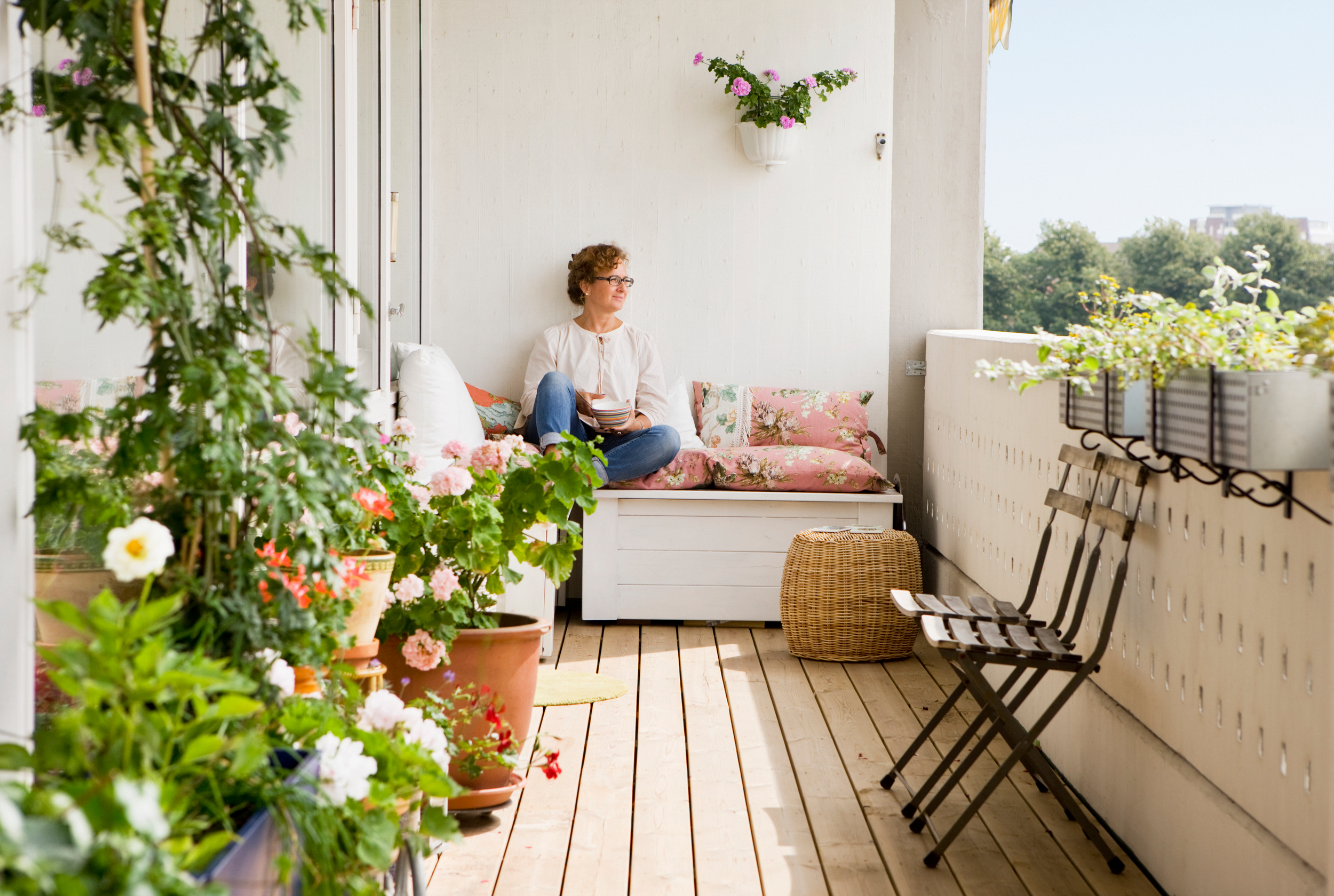 Kvinna njuter på sin balkong omgiven av växter en solig sommar dag. 