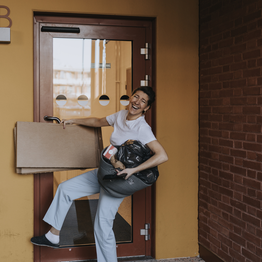 Glad kvinna på väg ut för att slänga kartonger och annat avfall i miljörummet